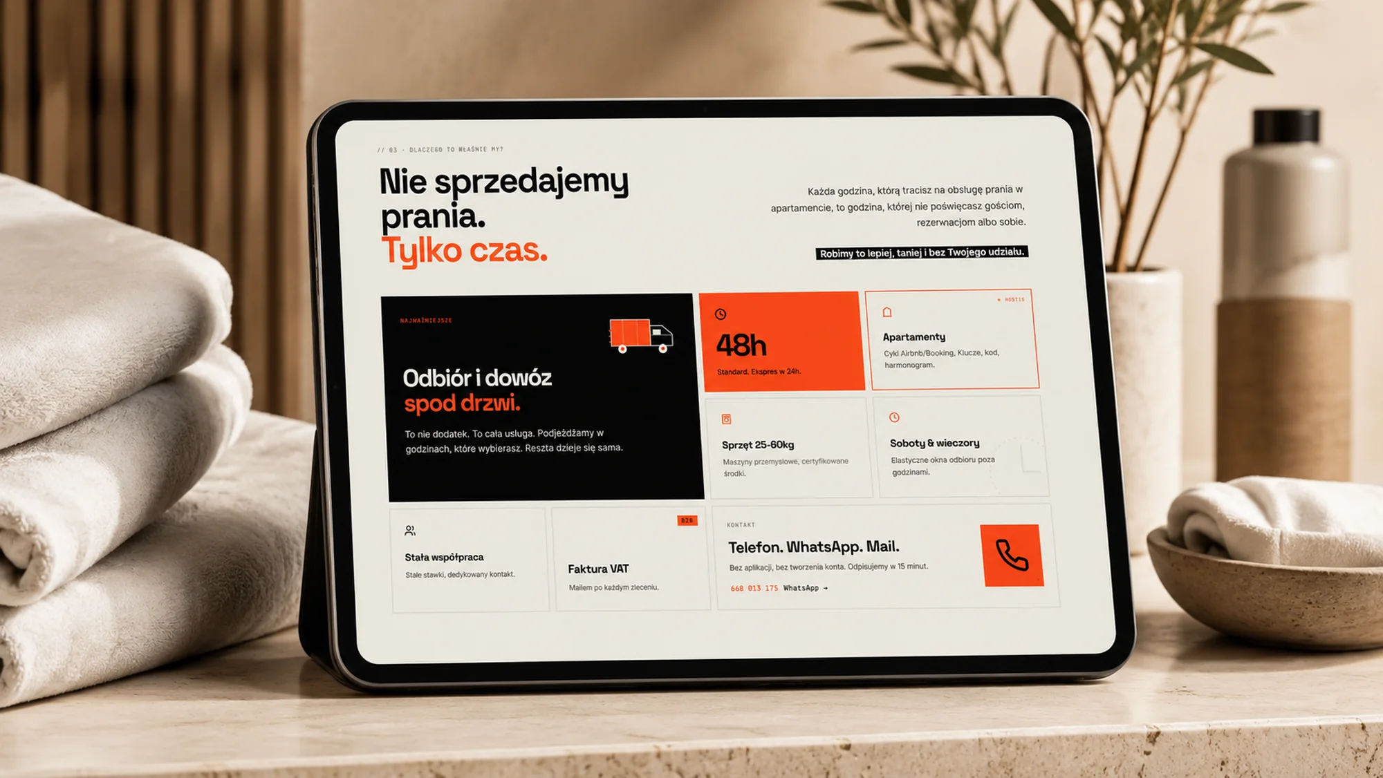 Sekcja „Nie sprzedajemy prania. Tylko czas.” na tablecie stojącym na kamiennym blacie, obok złożone ręczniki
